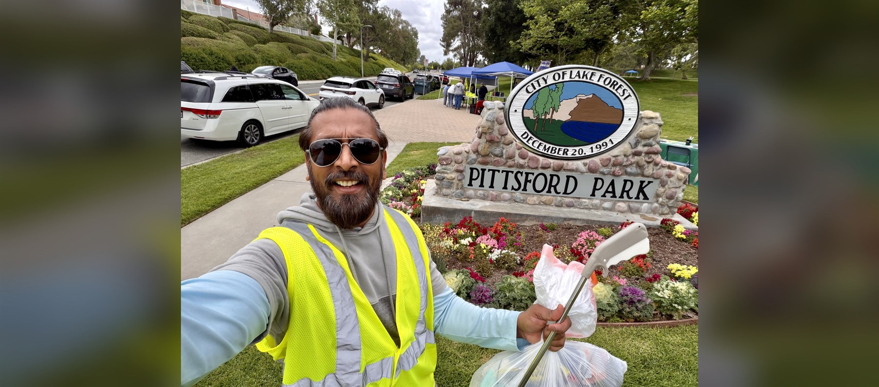 Anil Patel volunteering at Pittsford Park beside the City of Lake Forest park sign